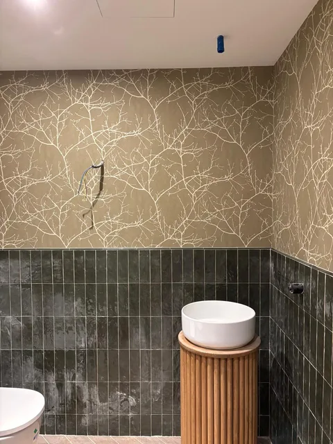 Papel pintado con ramas blancas sobre fondo oliva en un baño en proceso de acabado