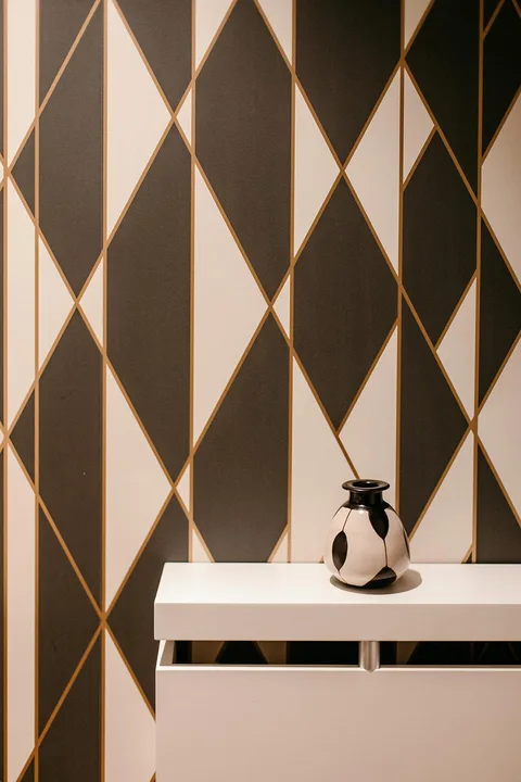Papel pintado de rombos en tonos oscuros y dorados sobre un mueble blanco